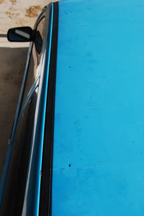 1991 Ford Festiva - A close-up view of a blue car's roof and side trim, with a side mirror attached.