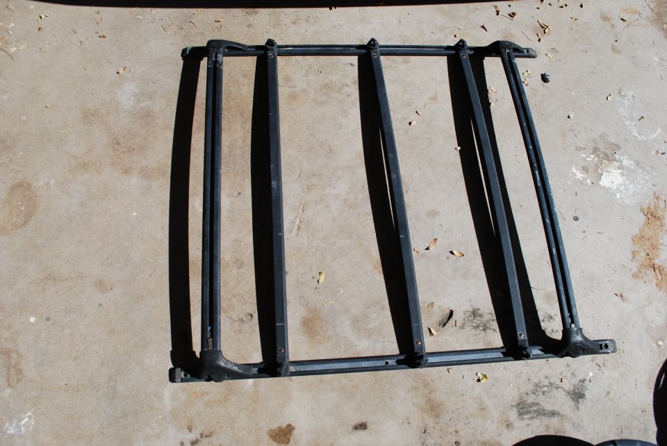 Black roof rack assembly with multiple crossbars and side rails, lying on concrete