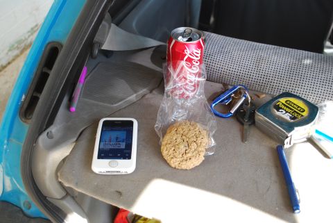 1991 Ford Festiva - A collection of items rests on a car's dashboard, including a cookie, a can of Coca-Cola, an iPhone, keys, and a tape measure.