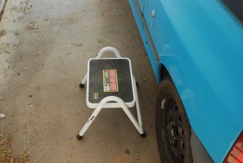1991 Ford Festiva - A blue car's side is visible next to a white step stool placed on a concrete surface.