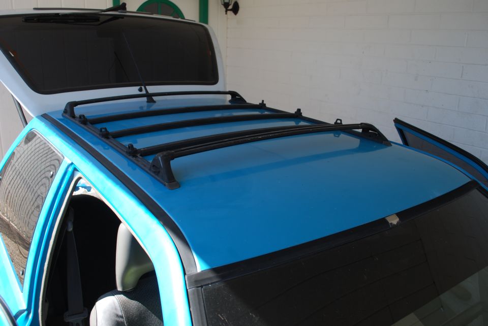 Blue vehicle roof with black cross-bar roof rack in a white brick garage