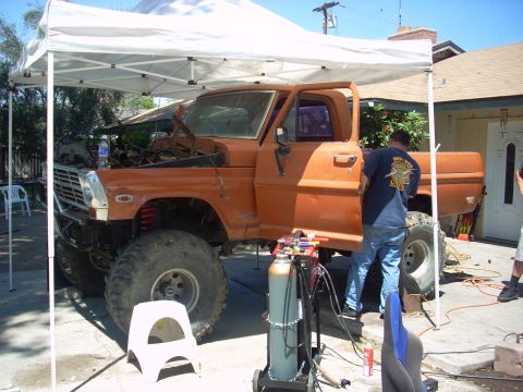 1992 Ford Ranger - An orange pickup truck is under a canopy, with a person working on the driver's side door and engine bay.