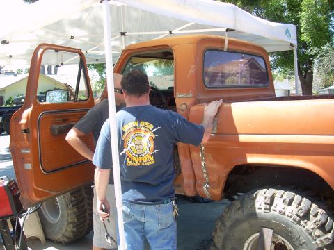 1992 Ford Ranger - An orange pickup truck with large off-road tires is examined by two men under a canopy.
