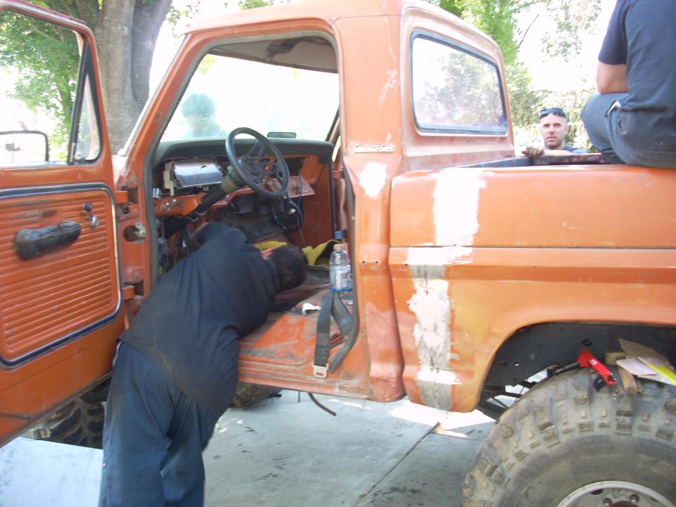 Man working on the interior of an orange pickup truck, driver's door open