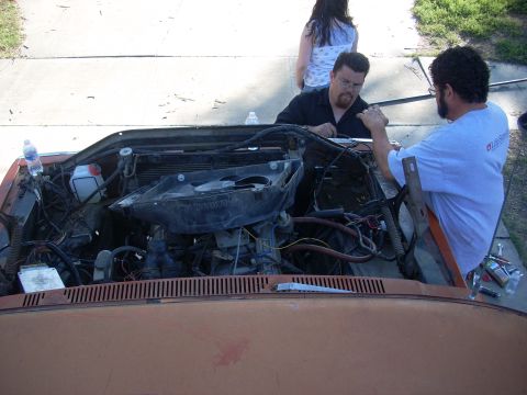 1992 Ford Ranger - Two men are working on the engine of an orange vehicle, with a woman standing in the background.