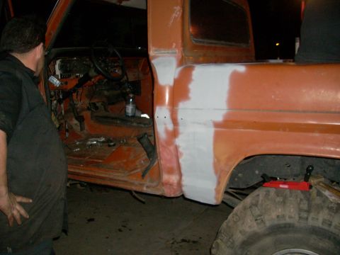 1992 Ford Ranger - A man looks into the open door of an orange pickup truck undergoing repairs.
