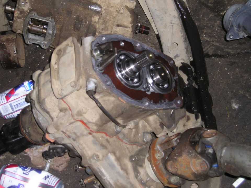 Disassembled transfer case with gears and bearings exposed, showing gasket material and some fluid. Two beer cans are visible on the left