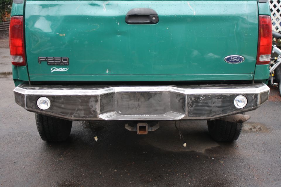 Rear view of a green 2003 Ford F-250 Super Duty with a custom metal bumper and tow hitch