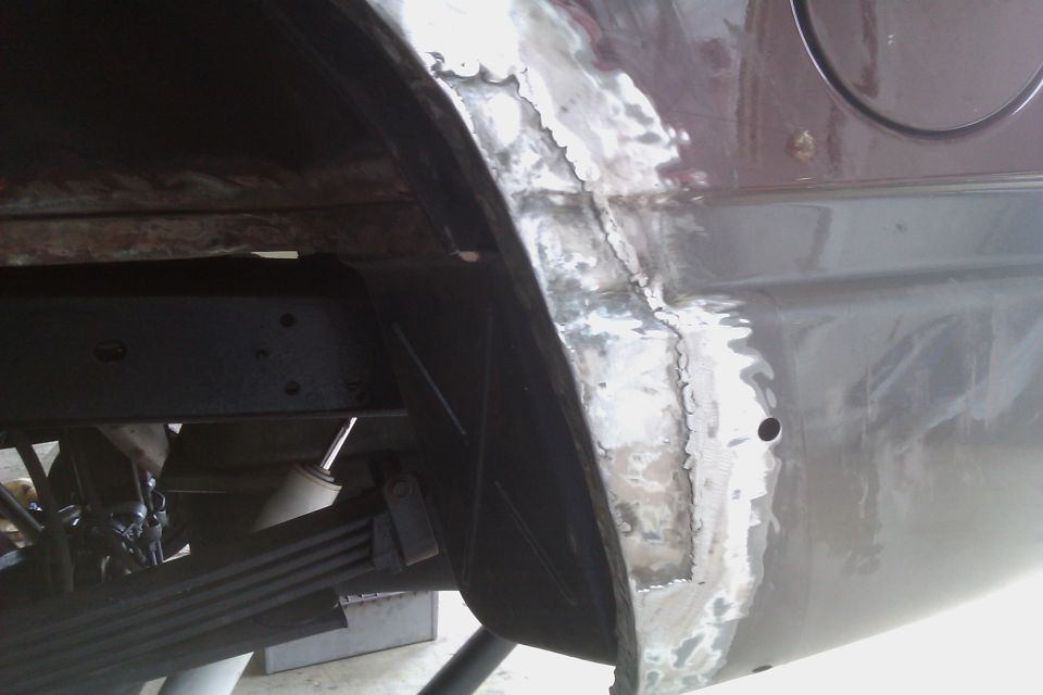 close-up of rusty wheel well area with metal patches and leaf springs visible