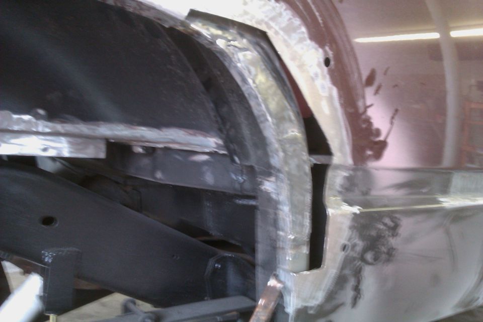 Close-up of rusty metal and frame repair on a vehicle's wheel well area. Some body filler is visible