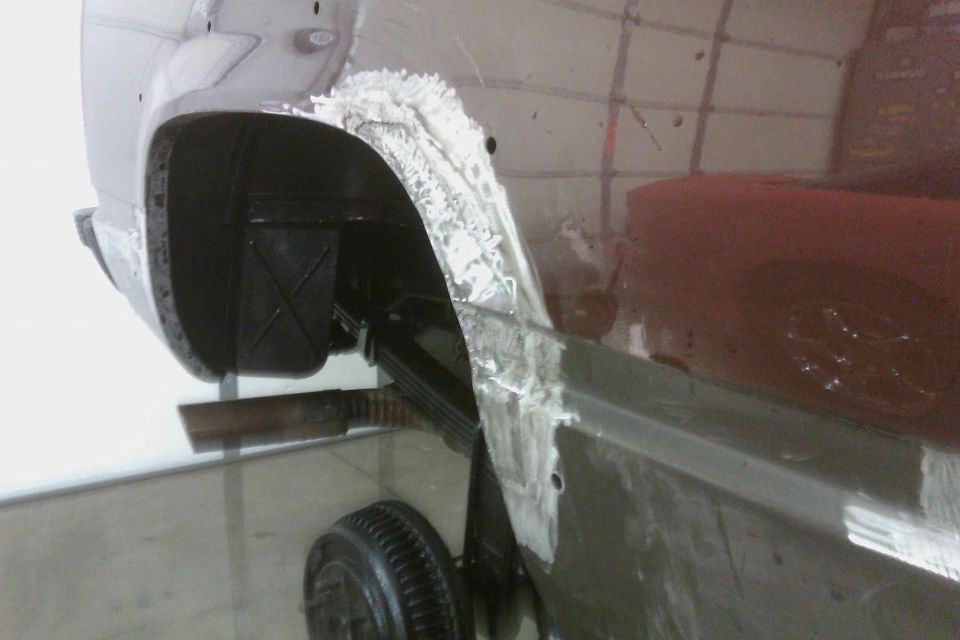 Dark red vehicle's rear wheel well and fender undergoing repair with body filler and primer
