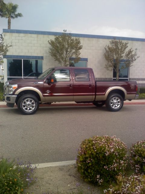 2011 Ford F-250 - A maroon pickup truck is parked outside a commercial building with trees and bushes nearby.