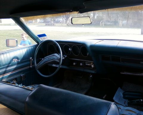 1976 Ford Torino - The interior of a 1976 Ford Torino shows blue seats and dashboard, with a child visible through the window.