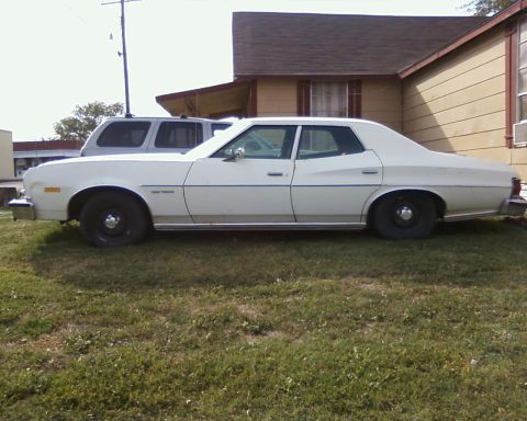 1976 Ford Torino - A white 1976 Ford Torino sedan is parked in front of a house, with an SUV visible behind it.