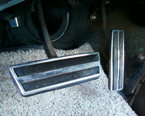 1976 Ford Torino - Close-up view of the accelerator and brake pedals inside a vehicle, showing the textured surfaces and chrome trim.