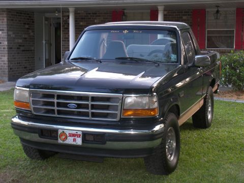 1996 Ford Bronco - A black Ford Bronco with tan trim is parked on a grassy lawn in front of a house.