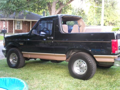 1996 Ford Bronco - Side profile of a black 1996 Ford Bronco with tan lower body trim, parked outdoors on a lawn.