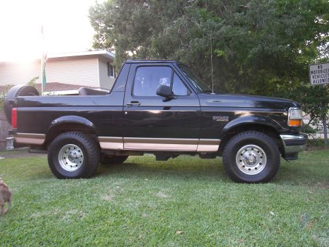 1996 Ford Bronco - A black Ford Bronco is parked on a grassy lawn in front of a house and trees.