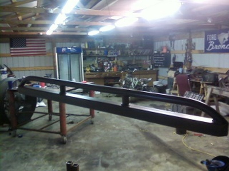 Pair of black metal rock sliders mounted on a red wheeled stand in a garage