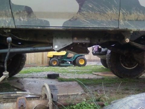 1995 Ford Bronco - The underside of a camouflaged SUV shows aftermarket rock sliders, with a lawnmower parked beneath.