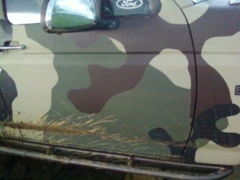 1995 Ford Bronco - Side view of a 1995 Ford Bronco door covered in camouflage paint, with mud on the rock slider.