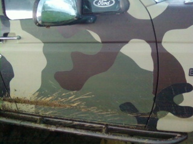 1995 Ford Bronco door with camouflage paint and mud splatter on rock slider