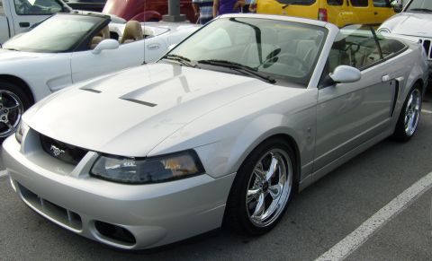 2007 Ford Mustang - A silver convertible Ford Mustang is parked next to other vehicles.