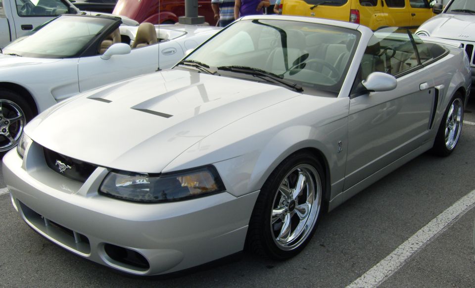 Silver convertible Ford Mustang with chrome wheels, hood scoops, and a black grille emblem