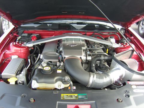 2007 Ford Mustang - The engine bay of a red Ford Mustang shows a prominent intake system and strut tower brace.