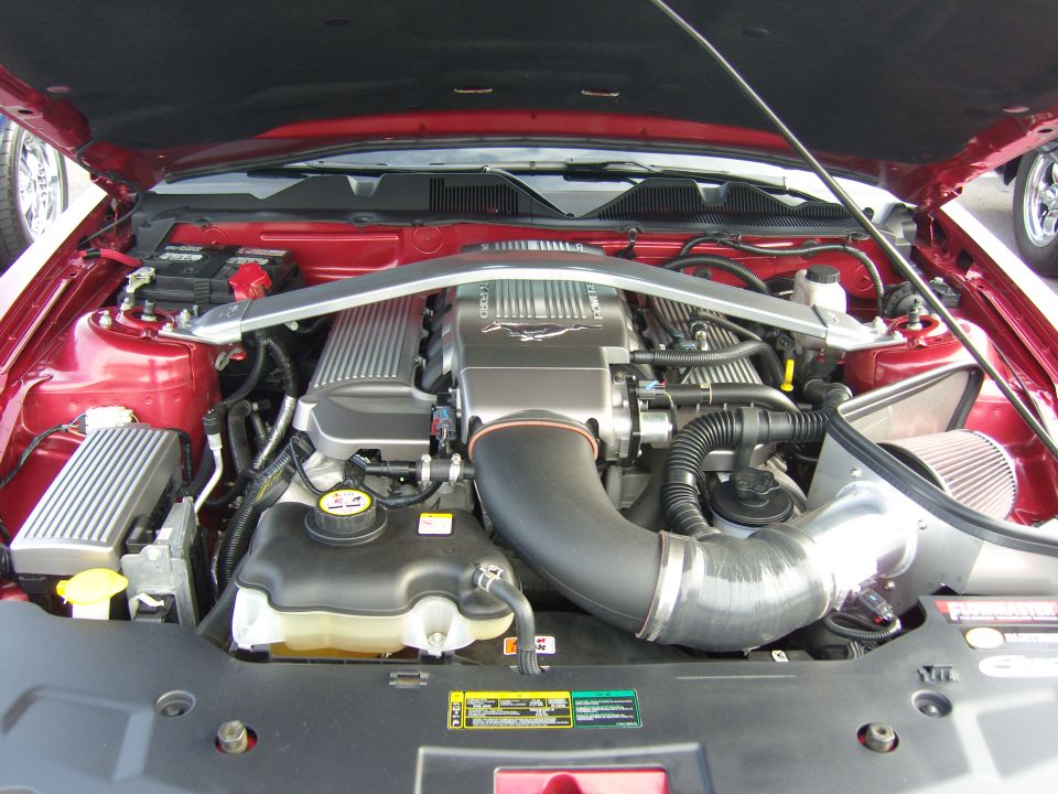 Red Ford Mustang engine bay with a silver strut tower brace and a large black intake tube