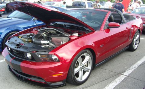 2007 Ford Mustang - A red 2007 Ford Mustang convertible is parked with its hood open, revealing the engine bay and racing stripes on the front.