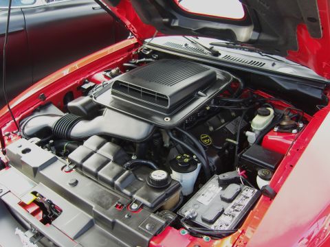 2007 Ford Mustang - The engine bay of a red 2007 Ford Mustang is visible with the hood raised, revealing the V8 engine and associated components.