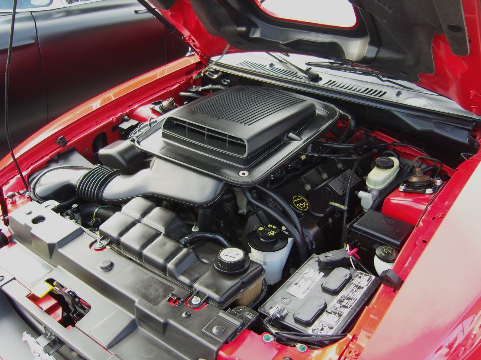 Red 2007 Ford Mustang engine bay with hood open. Shows V8 engine, air intake, battery, and fluid reservoirs