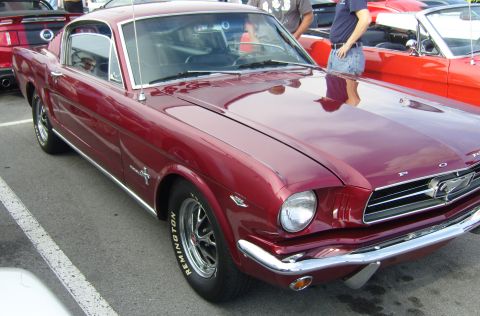 2007 Ford Mustang - A classic red 1965 Ford Mustang coupe is parked next to another red Mustang.