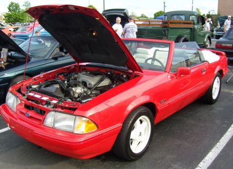 2007 Ford Mustang - Red convertible with hood open, parked at an outdoor event with other vehicles present.