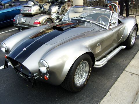 2007 Ford Mustang - A silver AC Cobra replica is parked outdoors next to other vehicles.