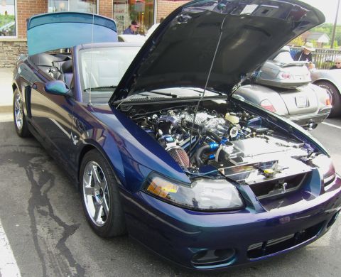 2007 Ford Mustang - A blue 2007 Ford Mustang convertible is parked with its hood open, revealing a supercharged engine.