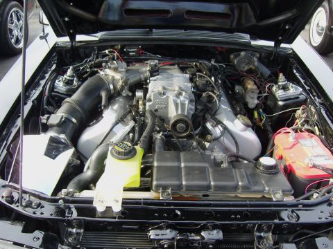 2007 Ford Mustang - Overhead view into the engine bay of a white Mustang with the hood raised, showing a Ford SVT supercharged modular V8 with cast intake, bla…
