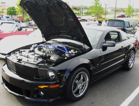 2007 Ford Mustang - Black S197 Ford Mustang coupe with a Roush body kit photographed at a car show with the hood raised, revealing a belt-driven supercharger w…