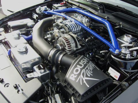 2007 Ford Mustang - Detailed engine bay shot of a Roush-built Mustang showing a Roughcharged supercharger with polished intercooler lid, a black Roush Racing a…