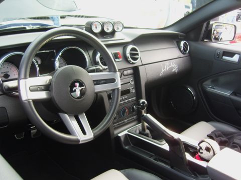 2007 Ford Mustang - Interior of an S197 Ford Mustang shot from the driver's door, showing the pony-badged three-spoke wheel, Roush-branded gauge cluster, a thr…