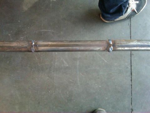 1995 Ford F-150 - A section of exhaust pipe with visible welds lies on a workshop floor, with a person's feet nearby.