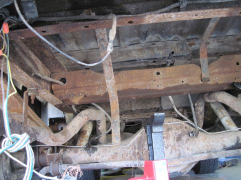 1979 Ford Bronco - The heavily rusted undercarriage of a vehicle is visible, showing the frame, exhaust, and suspension components.