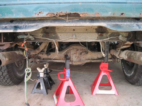 1979 Ford Bronco - The underside of a vehicle, supported by jack stands, reveals its rear axle, suspension, and exhaust system, with visible rust on the frame.