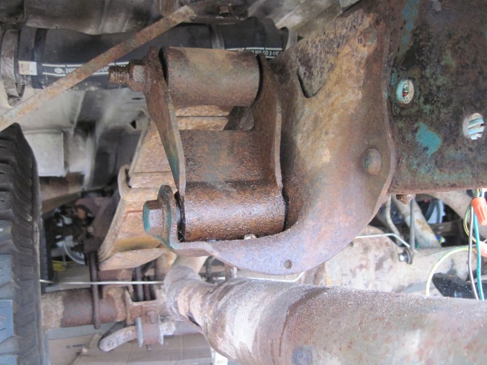 Close-up of heavily rusted suspension component and exhaust pipe, likely from an older vehicle