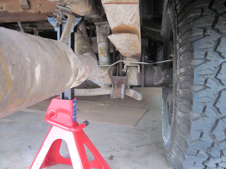 Rear axle and exhaust pipe supported by red jack stands under a vehicle