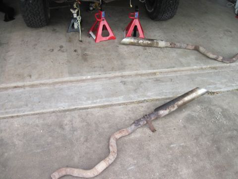 1979 Ford Bronco - Two removed exhaust pipes lie on the ground next to a vehicle supported by jack stands.