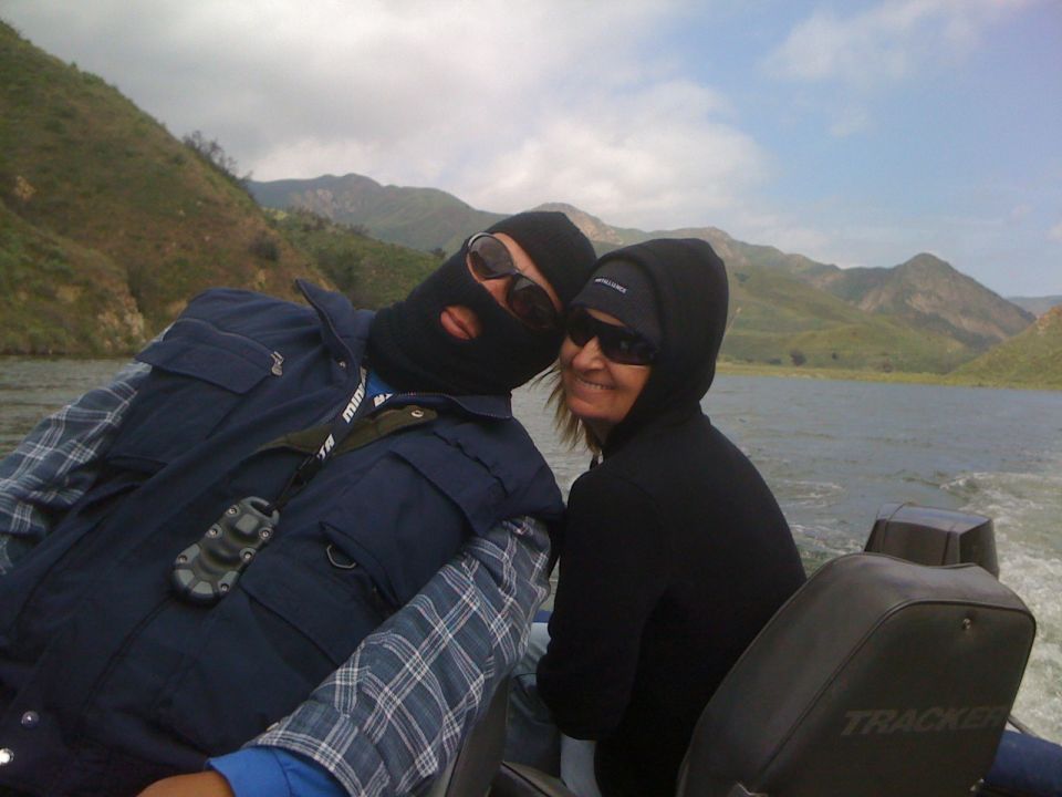 Two people wearing ski masks and sunglasses on a boat with mountains in the background