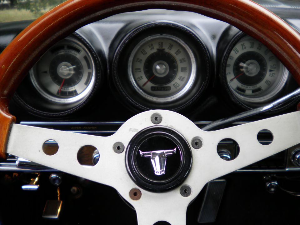 Classic car interior: wood steering wheel, bull-logo horn button, round chrome gauges