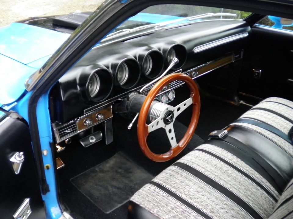 Classic car interior with wood steering wheel, black dash gauges, and striped bench seat